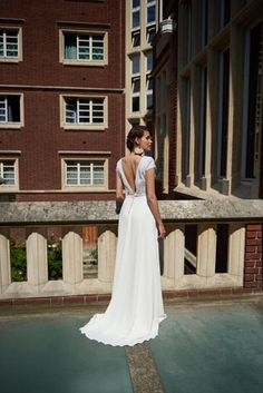 a woman in a white dress is standing on a ledge looking at the side of a building