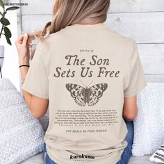 a woman sitting on a bed wearing a t - shirt that says the son sets us free