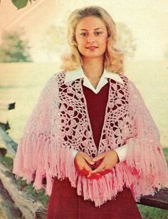 a woman wearing a pink crochet shawl with white collar and sleeves, standing in front of a lake