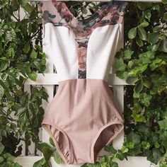 a pink and white swimsuit hanging on a wall with greenery in the background