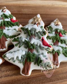 three decorated christmas tree cookies sitting on top of a wooden table