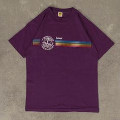 Women's Vintage 1980s Quinipet Single Stitch T-Shirt  + Damage: Nick To Front, Minor Marks/Lint Buildup  + Tag: Velva Sheen  + Made In USA  + Material: Cotton Blend  + Colour: Purple  + Size Label States: Small  + Recommended Size: Medium  + Measurements (Inches): Pit To Pit = 17, Body Length = 24  Please note that all vintage items have been previously worn, and may show some signs of previous wear. However, any significant damage will be photographed and/or stated in the items listing. Please Retro Purple T-shirt With Graphic Print, Vintage Purple Graphic Print Top, Retro Purple Crew Neck Top, Vintage Purple T-shirt With Letter Print, Vintage Purple T-shirt For Summer, Vintage Purple Cotton T-shirt, Colour Purple, Medium Purple, Size Label