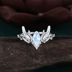 a ring with leaves and an opal stone in the center on top of a piece of wood