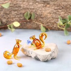 two glass figurines sitting on top of a rock next to nuts and leaves