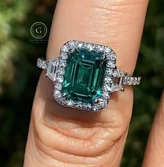 a woman's engagement ring with an emerald and diamond set in the center on her finger