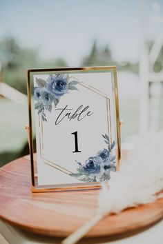 a table number with blue flowers on it and a white feather sitting next to it