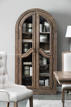 a white chair sitting in front of a wooden book shelf with glass doors on it