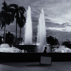 a person sitting on a bench in front of a fountain with water shooting from it