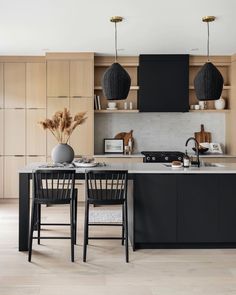 an open kitchen with black cabinets and wooden flooring on the walls, along with two bar stools