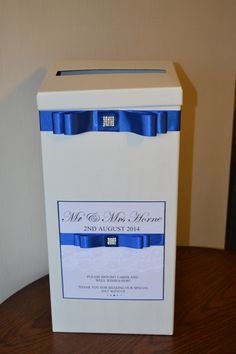 a white box with a blue ribbon on the front and back of it sitting on a wooden table