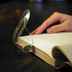 an open book with a magnifying glass on top of it next to a person's hand