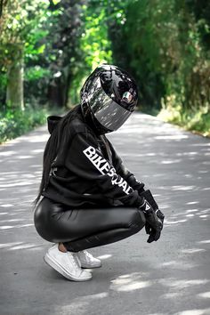 a person kneeling down on the side of a road wearing a motorcycle helmet and black leather pants