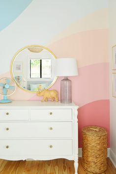 a white dresser topped with a mirror next to a pink and blue striped wallpaper