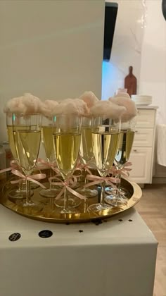 five champagne flutes are arranged on a gold platter with pink ribbons and cotton balls