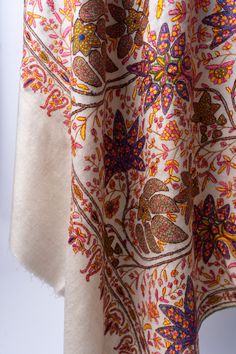 The Hand-Embroidered Sozni Garden Tapestry Pashmina Shawl is an opulent ode to the intricate gardens of the East. Artisans have hand-stitched a riot of floral majesty, with each petal and leaf crafted in vibrant saffron, amethyst, and ruby threads, across the shawl’s luxuriously soft cream pashmina. This shawl serves not merely as a garment but as a conversation with history, with every thread woven into a story of traditional Kashmiri splendor. It’s a garment destined for the wardrobes of those