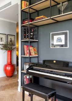 a living room with a piano and bookshelf next to a large red vase