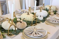 the table is set with white pumpkins, greenery and gold candlesticks