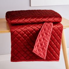 a red quilted blanket sitting on top of a wooden table next to a chair