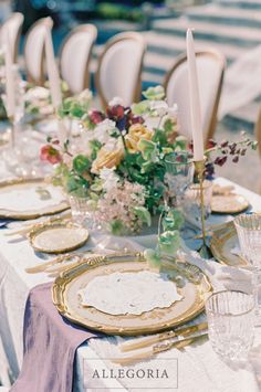 the table is set with gold and white plates, silverware, and floral centerpieces