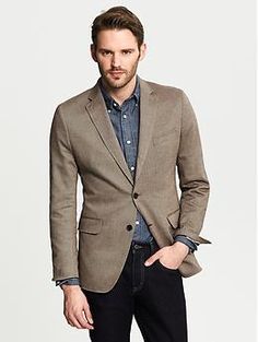 a man in a brown blazer is posing for the camera with his hands in his pockets