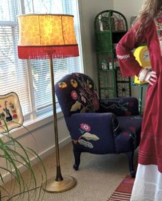 a woman standing in front of a window next to a blue chair and yellow lamp