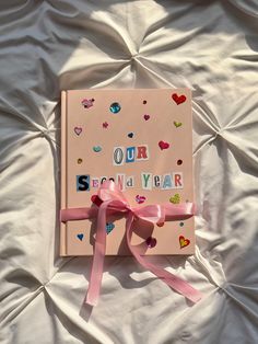 an open book with pink ribbon and confetti on it sitting on a bed