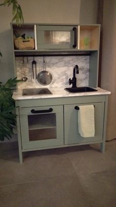 a toy kitchen with sink and cupboards in the corner, next to a potted plant