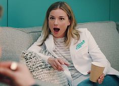 a woman sitting on a couch holding a coffee cup in her hand and making a surprised face