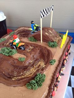 a birthday cake decorated with dirt bike tracks and race flags on the top, sitting on a checkered tablecloth