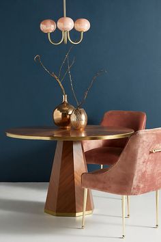 a dining room table with two chairs and a vase on the end, against a blue wall