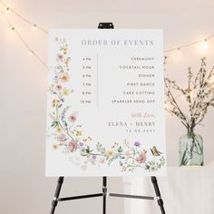 an order of events sign sitting on top of a easel next to a vase with flowers