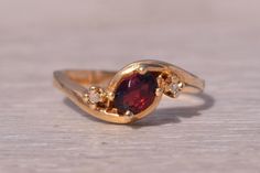 This stunning piece, known as The Garnet Whisper, features a captivating oval cut natural garnet at its center. The garnet is elegantly flanked by two round brilliant cut natural diamonds, adding a touch of sparkle and sophistication. The ring is crafted in 14 karat yellow gold and is currently a finger size 6.5 yet can be adjusted to any finger size for an additional charge upon request, ensuring a perfect fit. The ring bears a designer hallmark, yet we have not quite identified the maker yet. Ring Bear, Garnet And Diamond Ring, Garnet Rings, Gold Engagement Rings, Rings Statement, Oval Cut, Round Brilliant, Natural Diamonds, Statement Rings