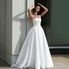 a woman in a white wedding dress leaning against a wall with her hand on her head