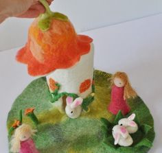 a hand is picking up the top of a felt doll house with rabbits and carrots on it