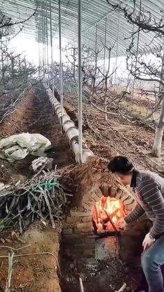 a woman standing over a fire pit in the middle of a forest