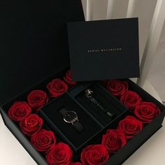 a black box filled with red roses next to a pair of watch and bracelets