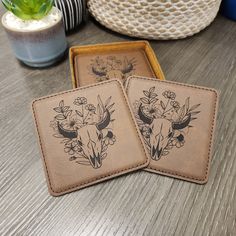 two coasters sitting on top of a wooden table next to a potted plant