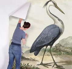 a woman is painting a large bird on the wall