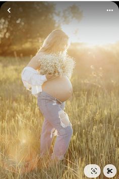 a pregnant woman standing in tall grass with her hands on her hips and the sun shining behind her