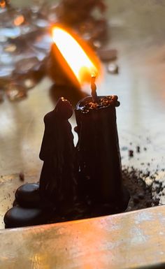 two small figurines sitting next to each other in front of a lit candle