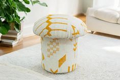 a white and yellow ottoman sitting on top of a rug next to a potted plant