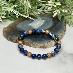 Experience the essence of harmony with the artisan-made Sodalite and Palm Wood Unisex Bracelet. This captivating accessory unites the tranquil allure of Sodalite and the rustic charm of Palm Wood, creating a wearable masterpiece that resonates with both elegance and earthy energy. Centered around the serene Sodalite beads, the bracelet showcases a palette of deep blues interwoven with delicate patterns, reminiscent of the vast expanse of a starlit sky. Sodalite is renowned for its ability to fos Adjustable Sodalite Beaded Bracelets With 8mm Beads, Adjustable Blue Earthy Jewelry, Bohemian Blue Stretch Bracelet For Meditation, Spiritual Sodalite Gemstone Beaded Bracelets, Sodalite Round Beads Bracelets For Healing, Adjustable Sodalite Gemstone Beaded Bracelets, Sodalite Beaded Bracelets With Natural Stones For Gift, Sodalite Round Beads Bracelets As Gifts, Spiritual Lapis Lazuli Beaded Bracelet With Natural Stones