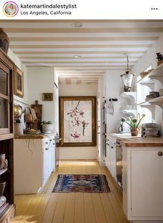 a long narrow kitchen with white cabinets and wood flooring is featured in this post