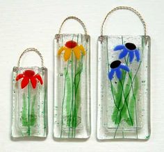 three glass vases with flowers in them sitting on a white surface, one is hanging from the wall