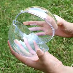 a person holding a clear plastic object in their hand on the grass with one hand reaching for it