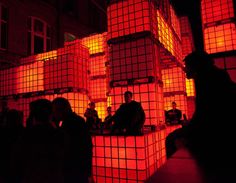 several people are sitting in front of red cubes on the wall at night time