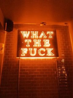 a neon sign that says what the fock is lit up in front of a brick wall