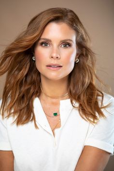 a woman with long hair wearing a white shirt and green necklace is looking at the camera