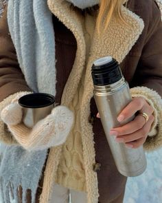 a woman holding a coffee cup in her hand and wearing a scarf around her neck