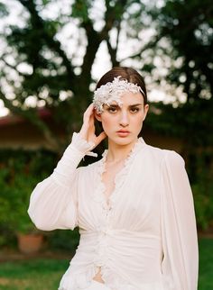 a woman in a white dress is holding her hair up to her face and posing for the camera